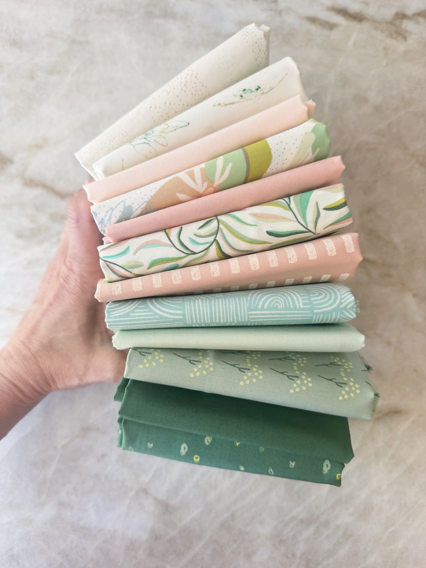 Stack of colorful fabric bundles held by a hand on a neutral background