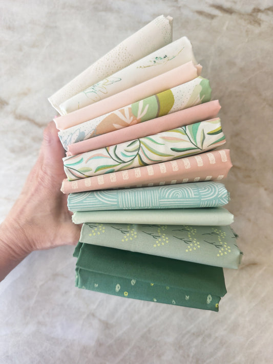 Stack of colorful fabric bundles held by a hand on a neutral background