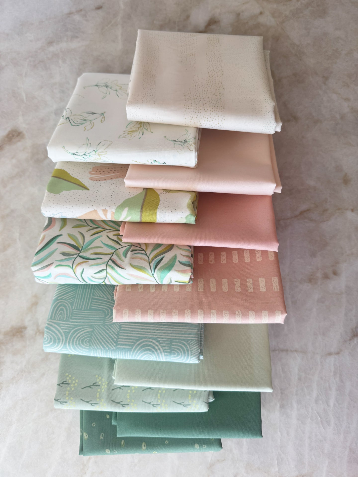 Stack of folded fabric swatches in various patterns and colors on a marble surface