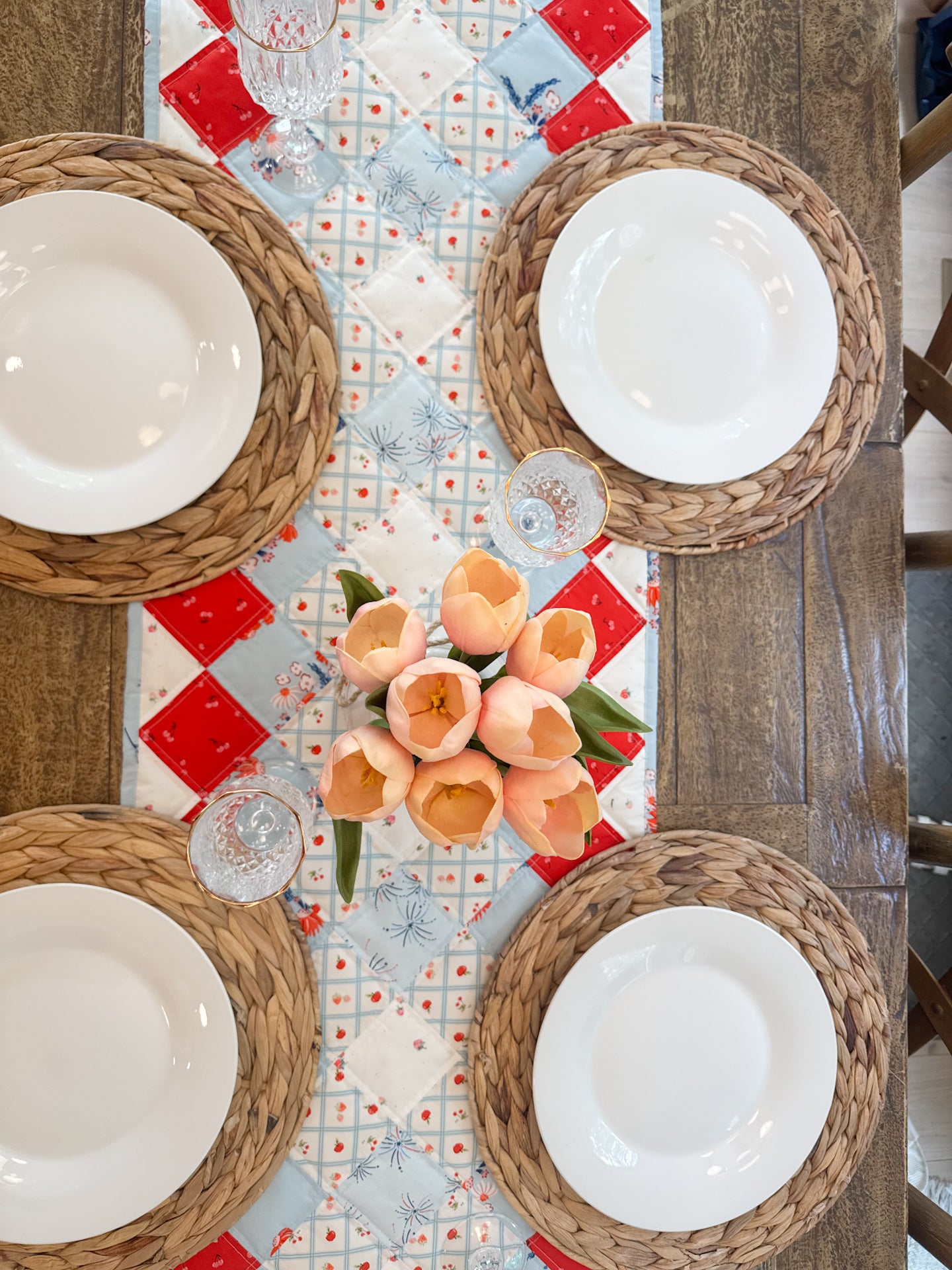 Table setting with woven coasters, white plates, and a floral arrangement on a patterned tablecloth.