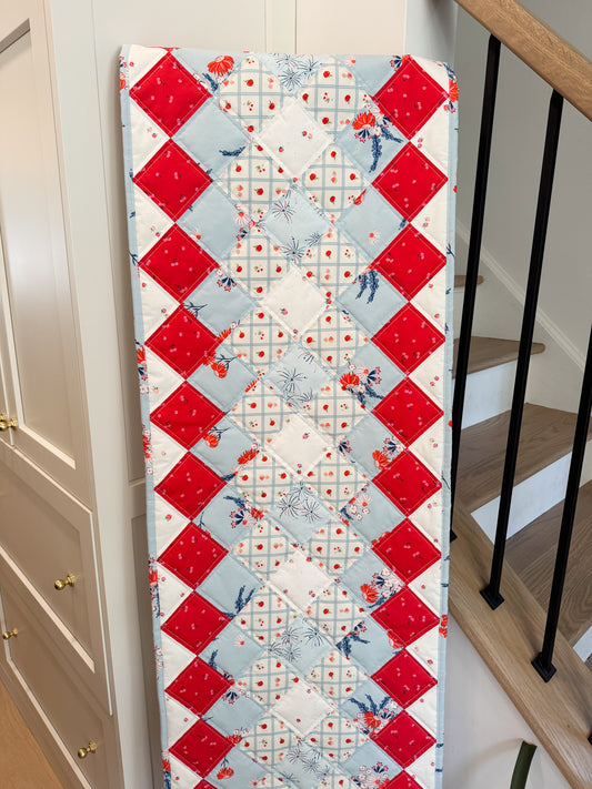 Quilt with red, white, and blue diamond pattern on a wooden table.