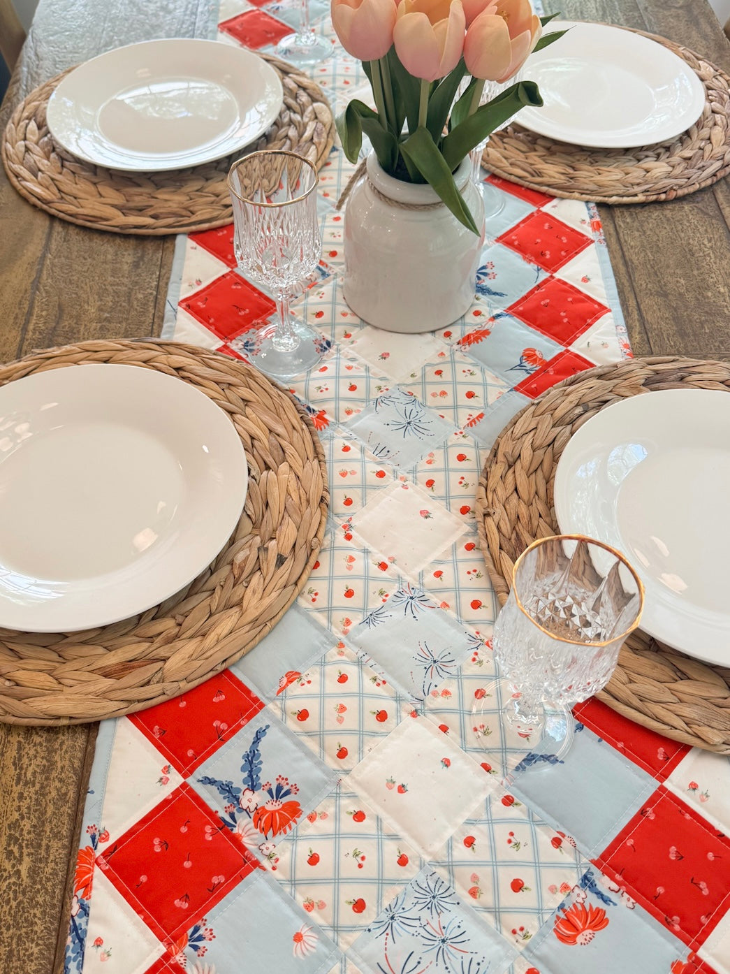 Dining table set with a patchwork tablecloth, plates, glasses, and tulips.