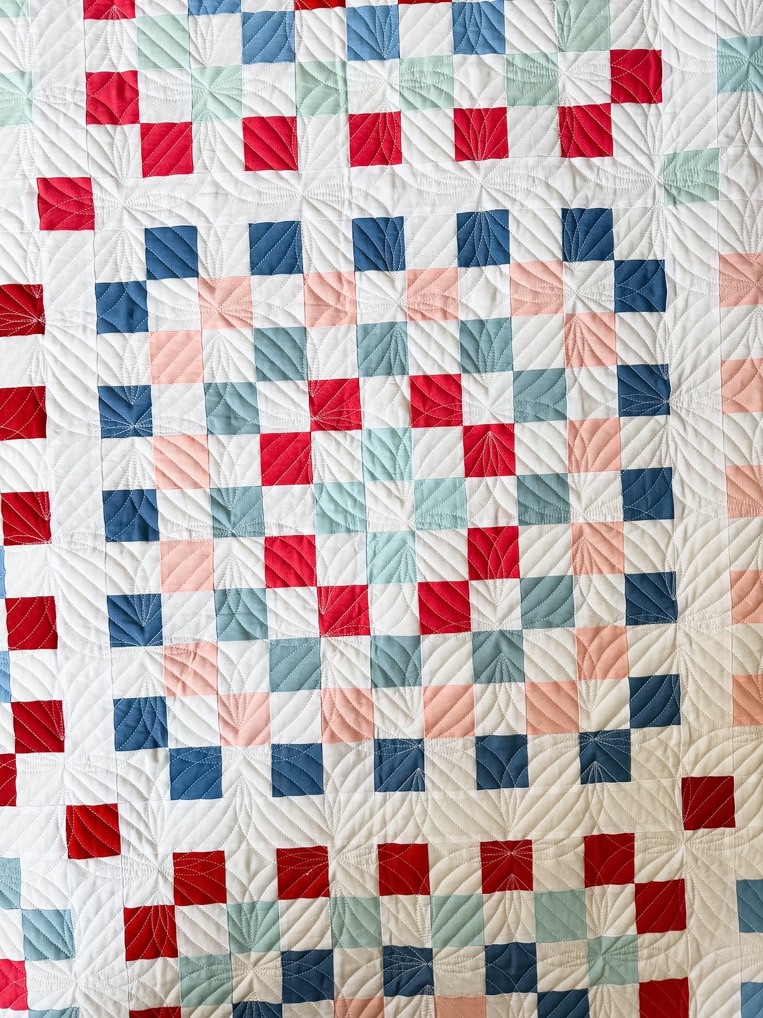 Quilt with a patchwork pattern of red, blue, and pink squares on a white background