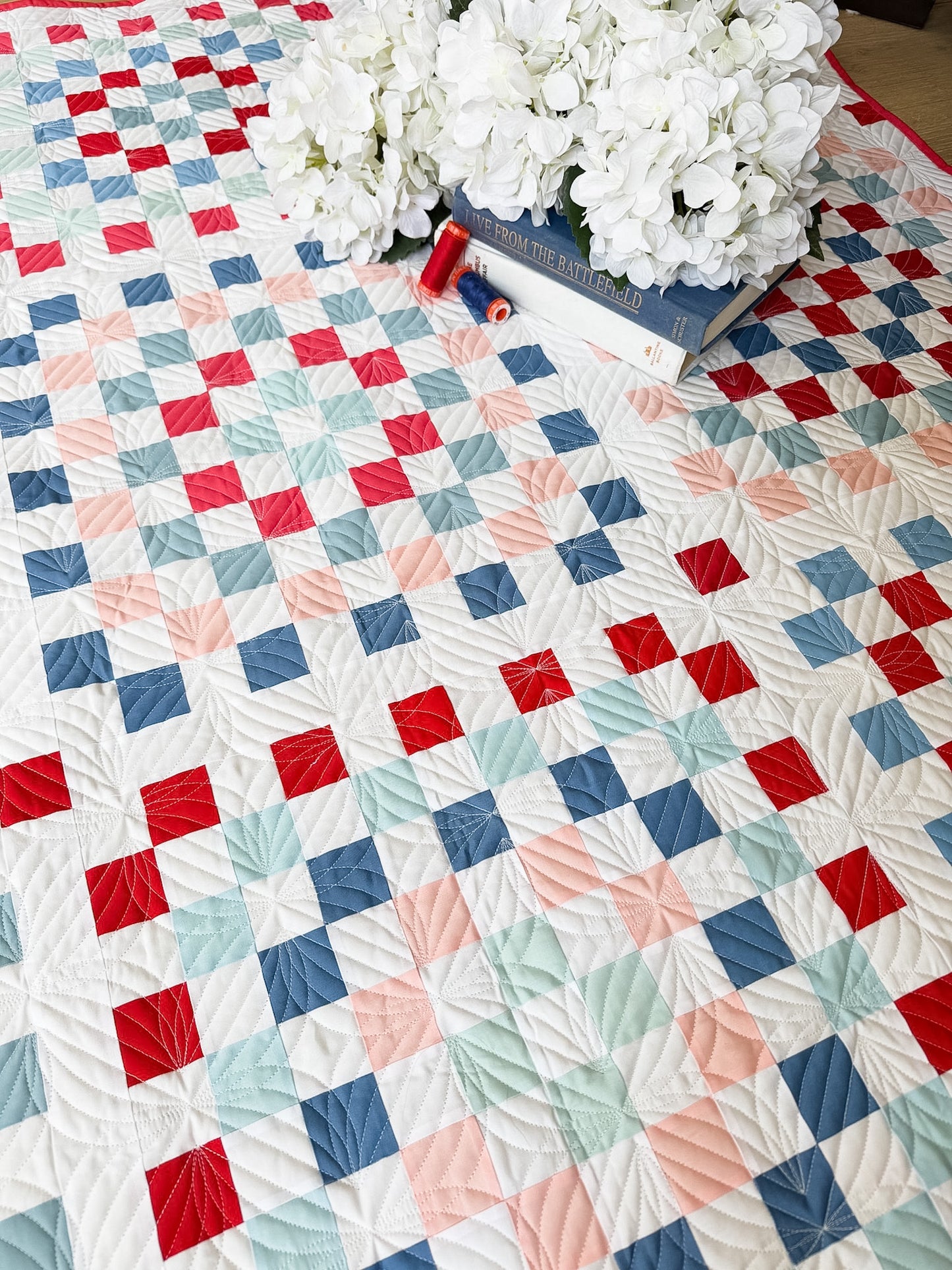Quilt with a geometric pattern featuring red, blue, and pink squares on a white background.
