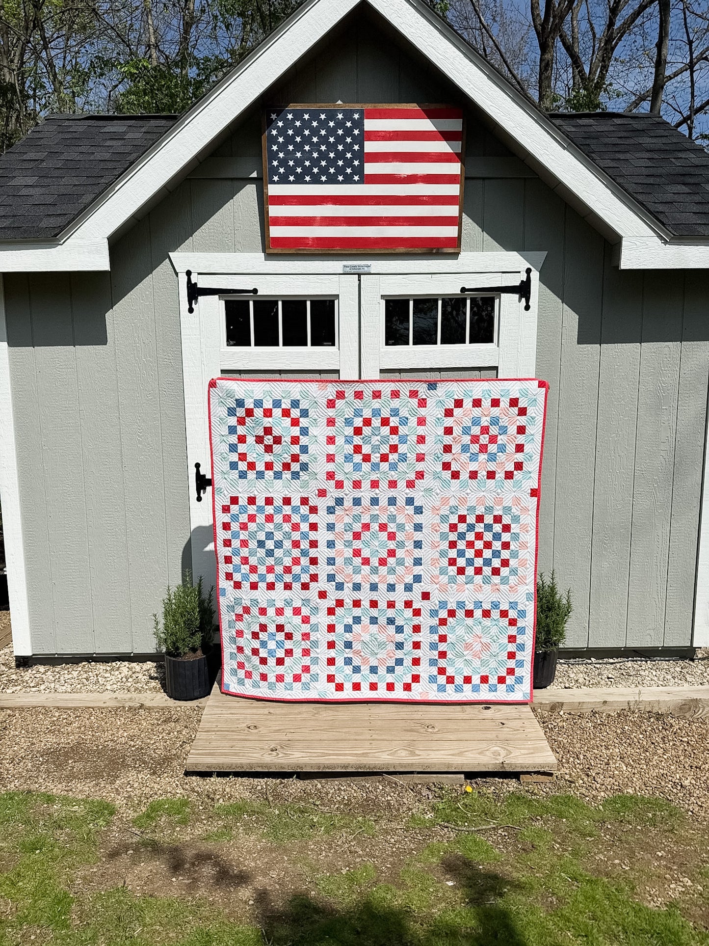 Quilt with a geometric pattern displayed in front of a building with an American flag.